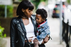 Mujer negra sosteniendo a un niño pequeño y caminando por una calle de la ciudad.
