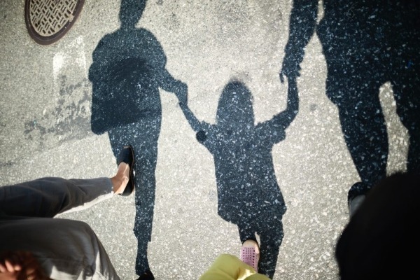Sombra de dos adultos caminando por un paso de peatones y tomados de la mano con un niño pequeño entre ellos.