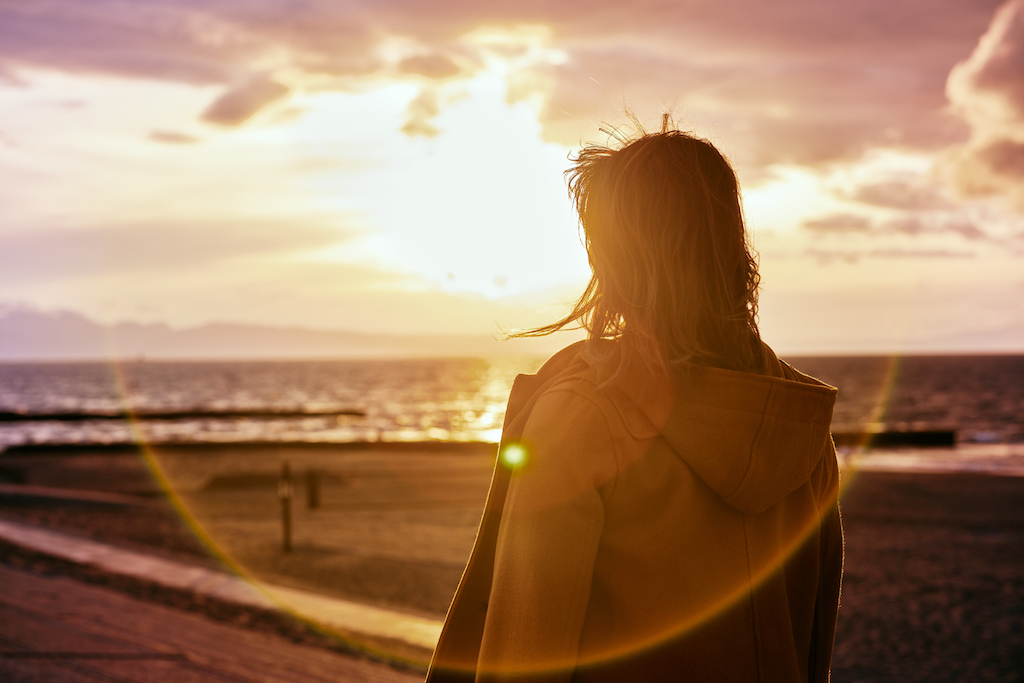 A young woman looking out on the beach at sunset