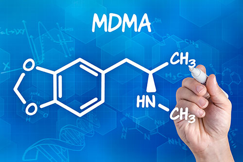 Una mano escribiendo la estructura química de la MDMA en una pizarra