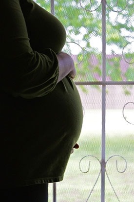 お腹を抱えて窓の外を見ている妊婦さんの写真