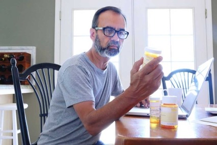 Hombre sentado en la mesa del comedor mirando la etiqueta de un frasco de medicamento recetado.