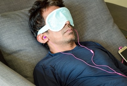 Man on his back laying on a couch wearing an eye mask and wired earbuds during a therapy session.