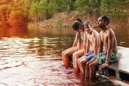 Grupo de amigos adolescentes sentados en un muelle sobre un lago